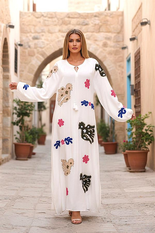 Beyaz renkli, önü ve kolları renkli nakış işlemeli, püskül bağlamalı uzun viskon elbise.