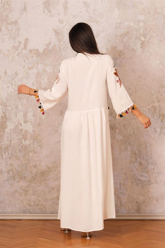 A woman wears a long white V-neck dress with authentic embroidery and tassels on the sleeves.