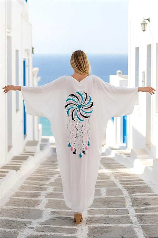 Sırtında renkli nakış işlemeleri bulunan, beyaz, V yaka, uzun ve oversize kadın elbisesi.