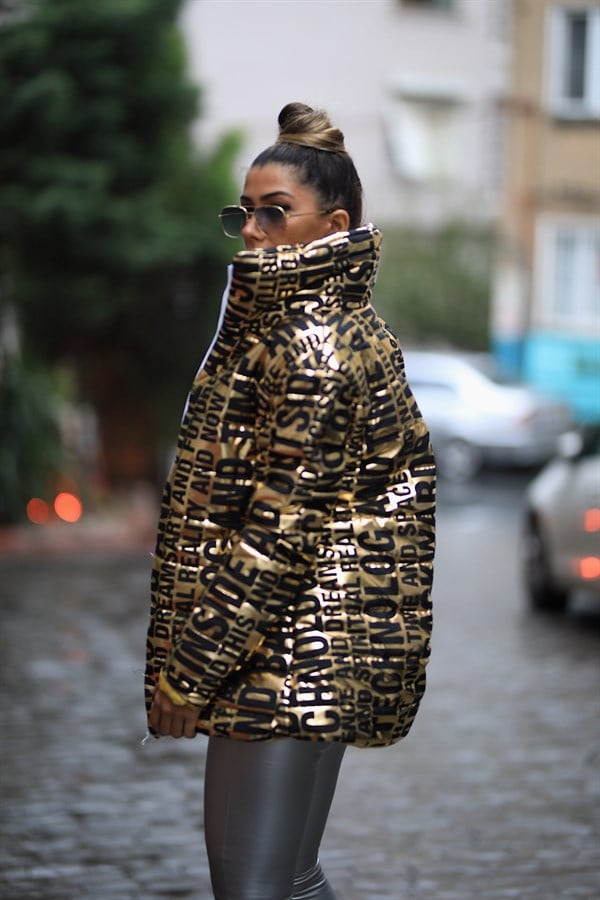 Siyah yazılı desenlere sahip, dik yakalı, parlak gold renkli uzun şişme mont.