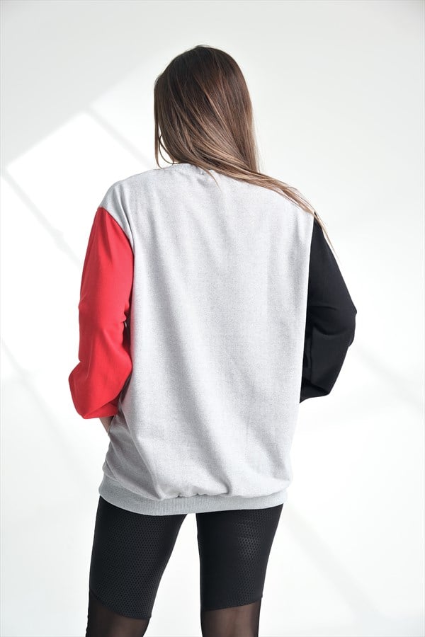 Gri renkli, kırmızı ve siyah kollu, kanguru cepli sweatshirt giyen bir kadın.