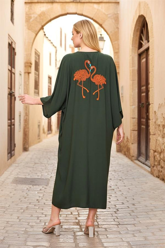 A woman wears an oversized khaki V-neck dress featuring flamingo embroidery on the back.