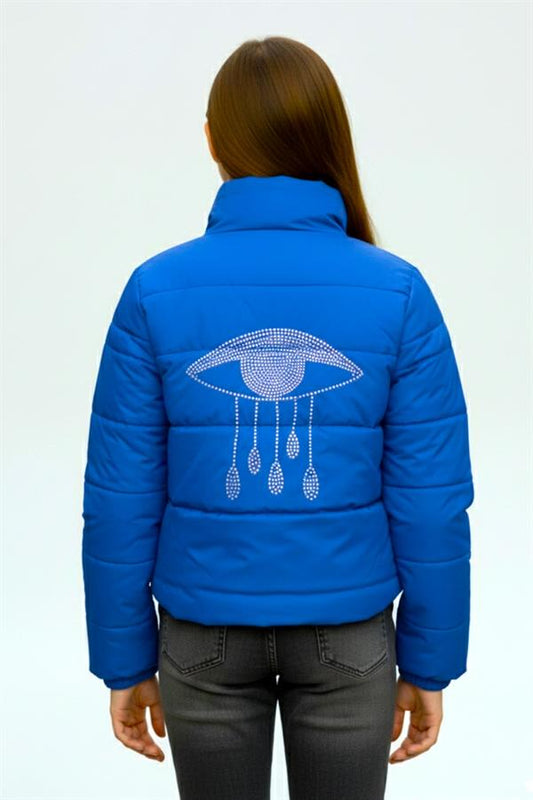 Saks mavisi, dik yakalı, sırtında taş işlemeli göz detayı bulunan kız çocuk şişme mont.