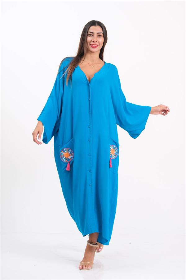 A woman wears a long, blue, button-down oversize dress with embroidered pockets and tassels.