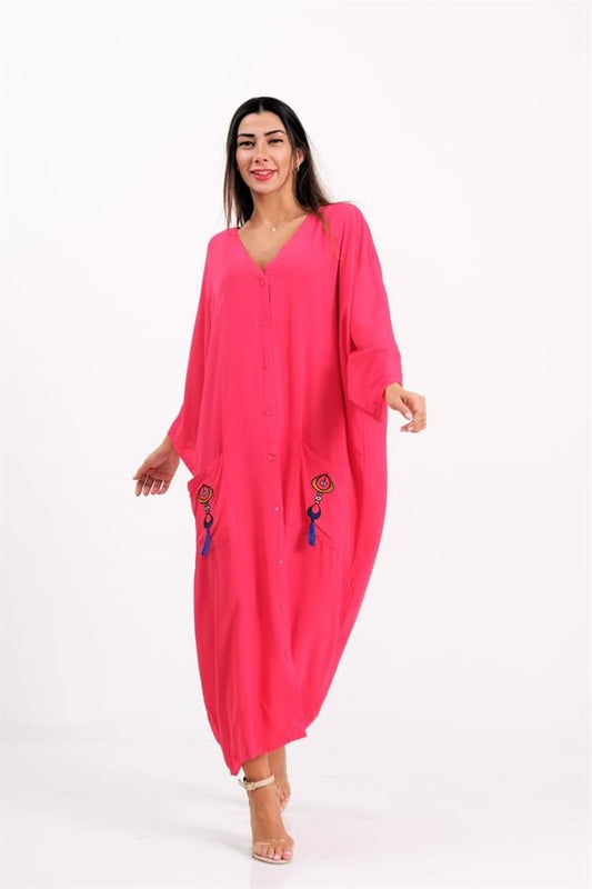 A woman wears a pink oversized button-down dress with embroidered pockets and tassel details.