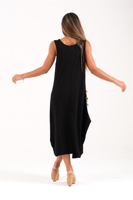 A woman wearing a black sleeveless long dress with tassel-detailed pockets seen from behind.
