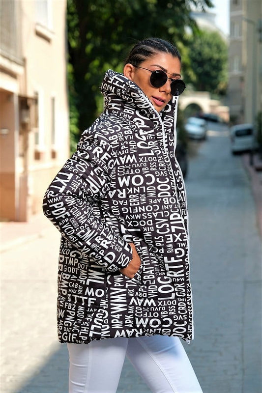 Siyah beyaz harf desenli, dik yakalı ve uzun şişme mont giyen bir kadın.