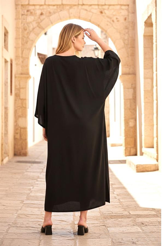 Siyah, oversize, uzun kollu ve yan yırtmaçlı viskon elbise giyen bir kadın.