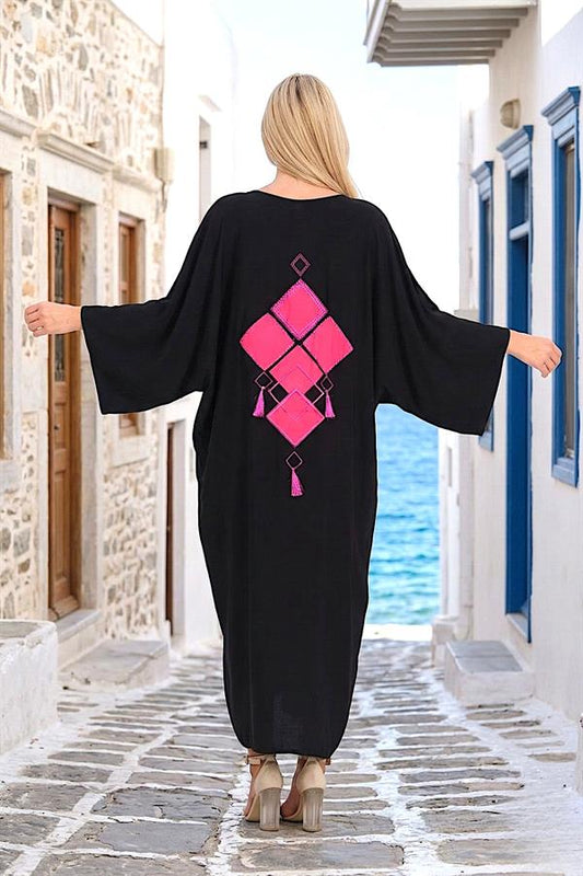 Sırtında pembe nakışlı ve püsküllü detaylar bulunan siyah oversize uzun gömlek elbise.