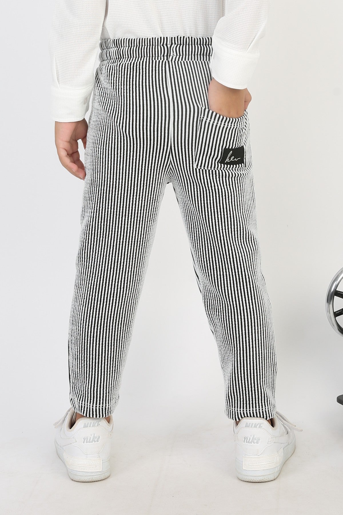 Arka cebinde arma detayı bulunan, siyah beyaz çizgili, fitilli kumaştan erkek çocuk pantolonu.