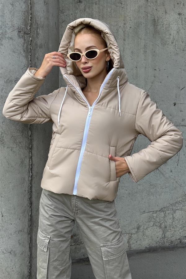 Bej renkli, kapüşonlu, beyaz fermuarlı ve su geçirmez kumaştan üretilmiş şişme mont.
