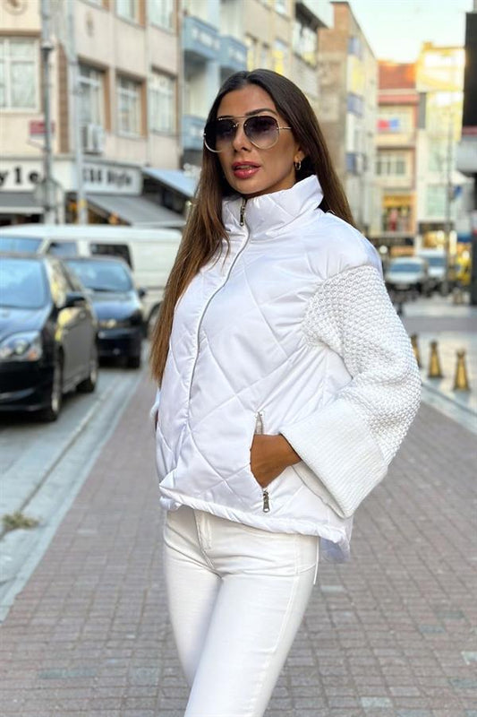 Beyaz dik yakalı, fermuarlı, triko kollu ve cepli şişme mont.