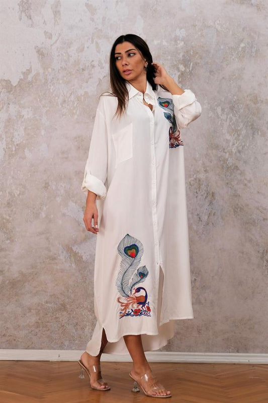 Beyaz, göğüs ve etek kısmında tavus kuşu nakışları bulunan, cepli ve uzun gömlek elbise.