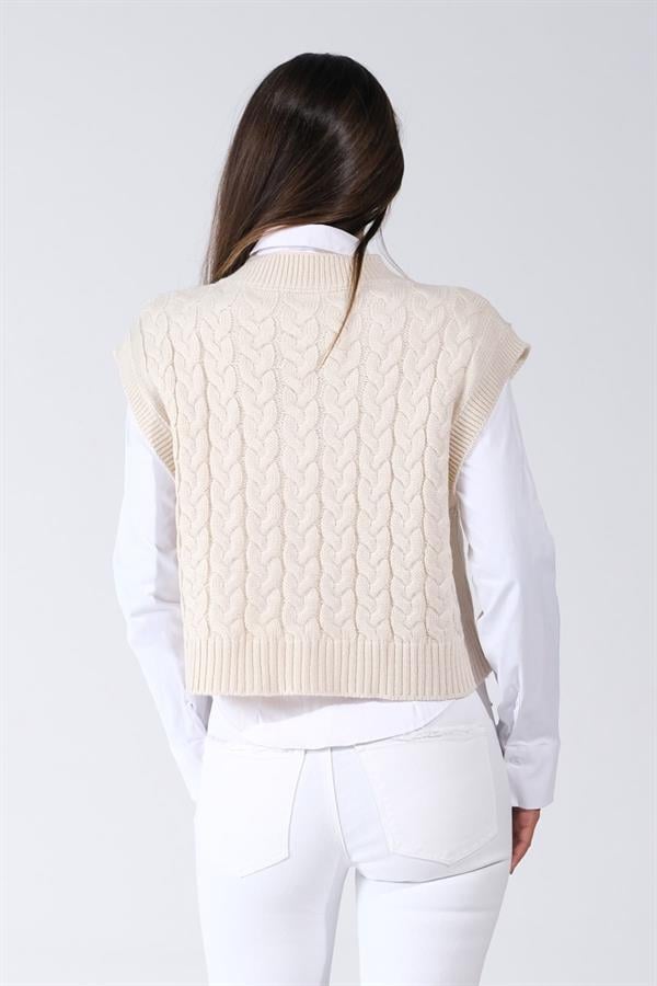 Beyaz V yaka saç örgülü crop triko süveter giyen bir kadın.