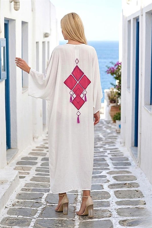 Sırtında pembe nakışlı ve püsküllü detaylar bulunan, beyaz, oversize uzun gömlek elbise.