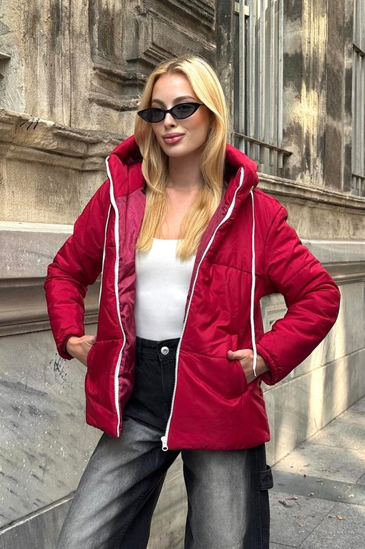 Beyaz içlik ve gri kot pantolon ile kombinlenmiş bordo renkli, kapüşonlu şişme mont.
