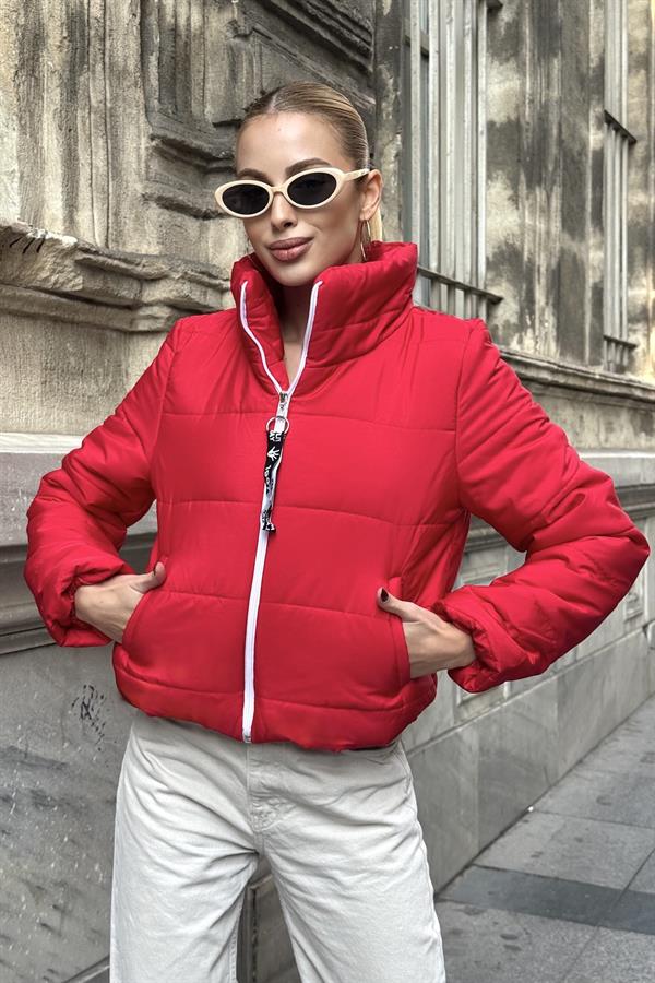 Beyaz fermuarlı, dik yakalı, kırmızı kısa şişme mont giyen bir kadın.