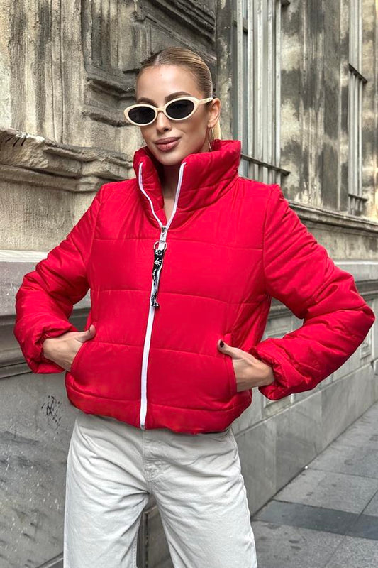 Beyaz fermuarlı, dik yakalı, kırmızı kısa şişme mont giyen bir kadın.