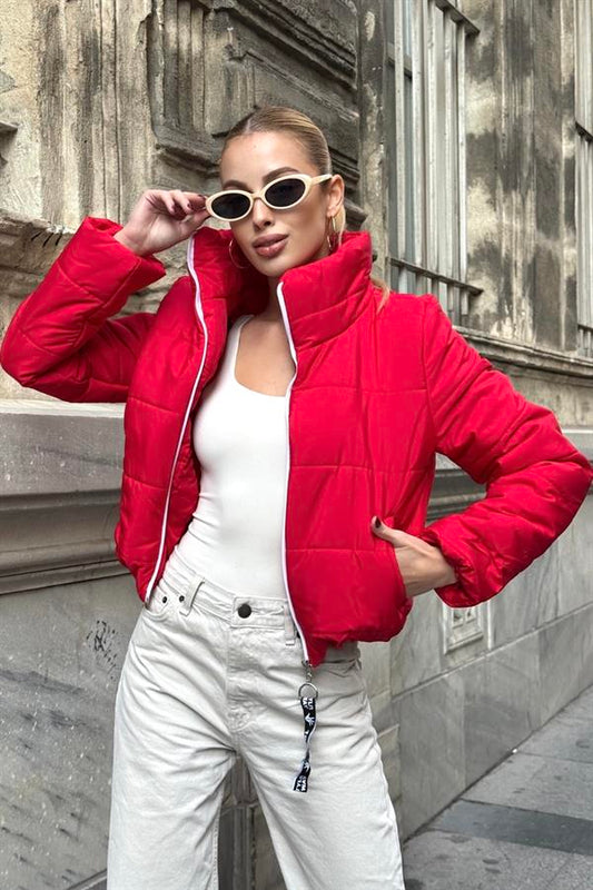 Beyaz içlik ve açık renkli pantolon ile kombinlenmiş, dik yakalı, kırmızı kısa şişme mont.