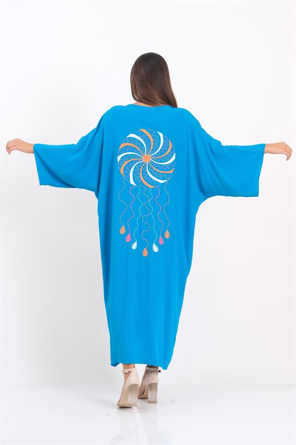A woman wears a long, blue, oversized V-neck dress featuring a colorful embroidered design on the back.