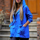 Saks mavisi, kapüşonlu, fermuarlı ve cepli ince kadın yağmurluk.