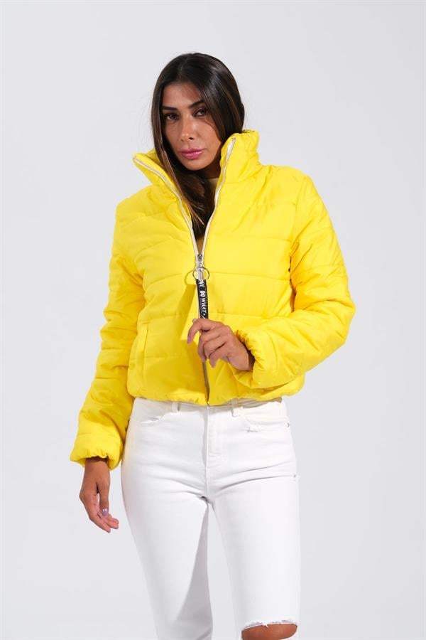 Sarı renkli, dik yakalı, kısa kesim şişme mont giyen bir kadın.