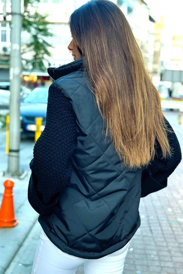 Siyah dik yakalı, kolları triko detaylı ve kapitone desenli şişme mont.