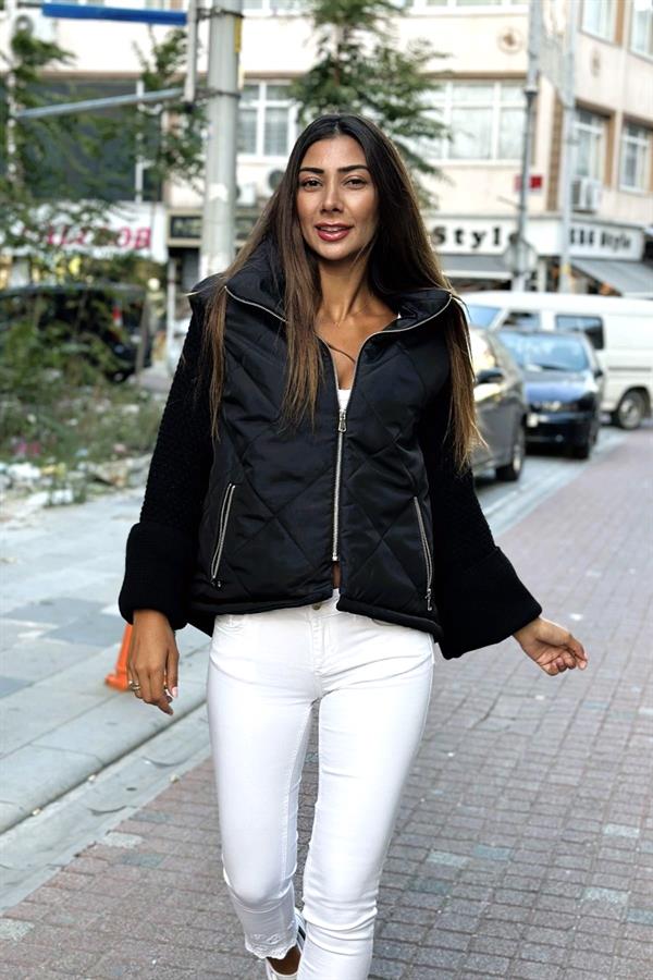 Siyah dik yakalı, fermuarlı, şişme gövdeli ve triko kollu kadın mont.