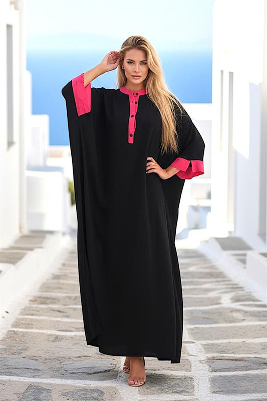 Pembe detaylı, düğmeli, yarasa kollu, siyah oversize uzun elbise giyen bir kadın.
